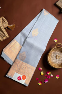 Light blue saree with gold patterns on a brown surface with wicker baskets and rose petals.