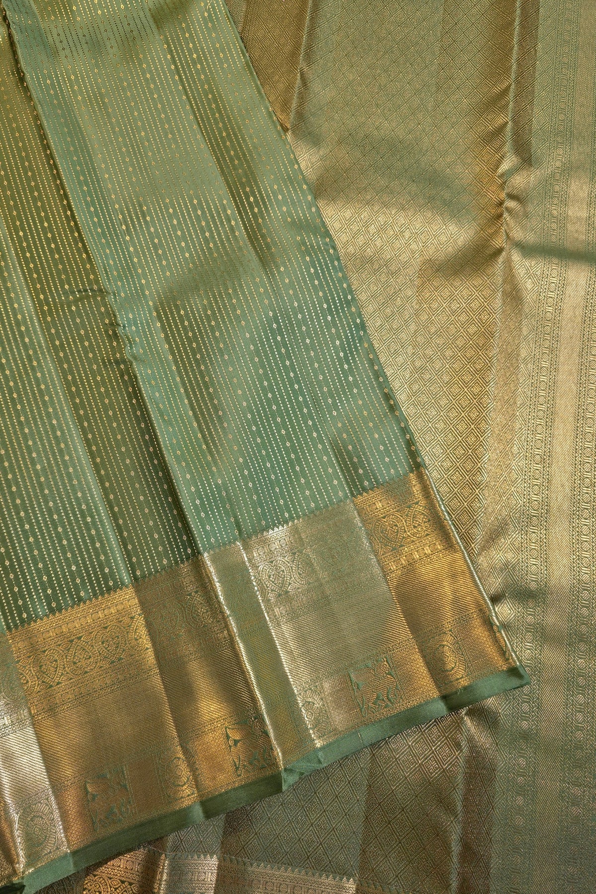 A close-up of a green and gold zari woven fabric, likely a saree, showing the body fabric, border, and detailed metallic embroidery.