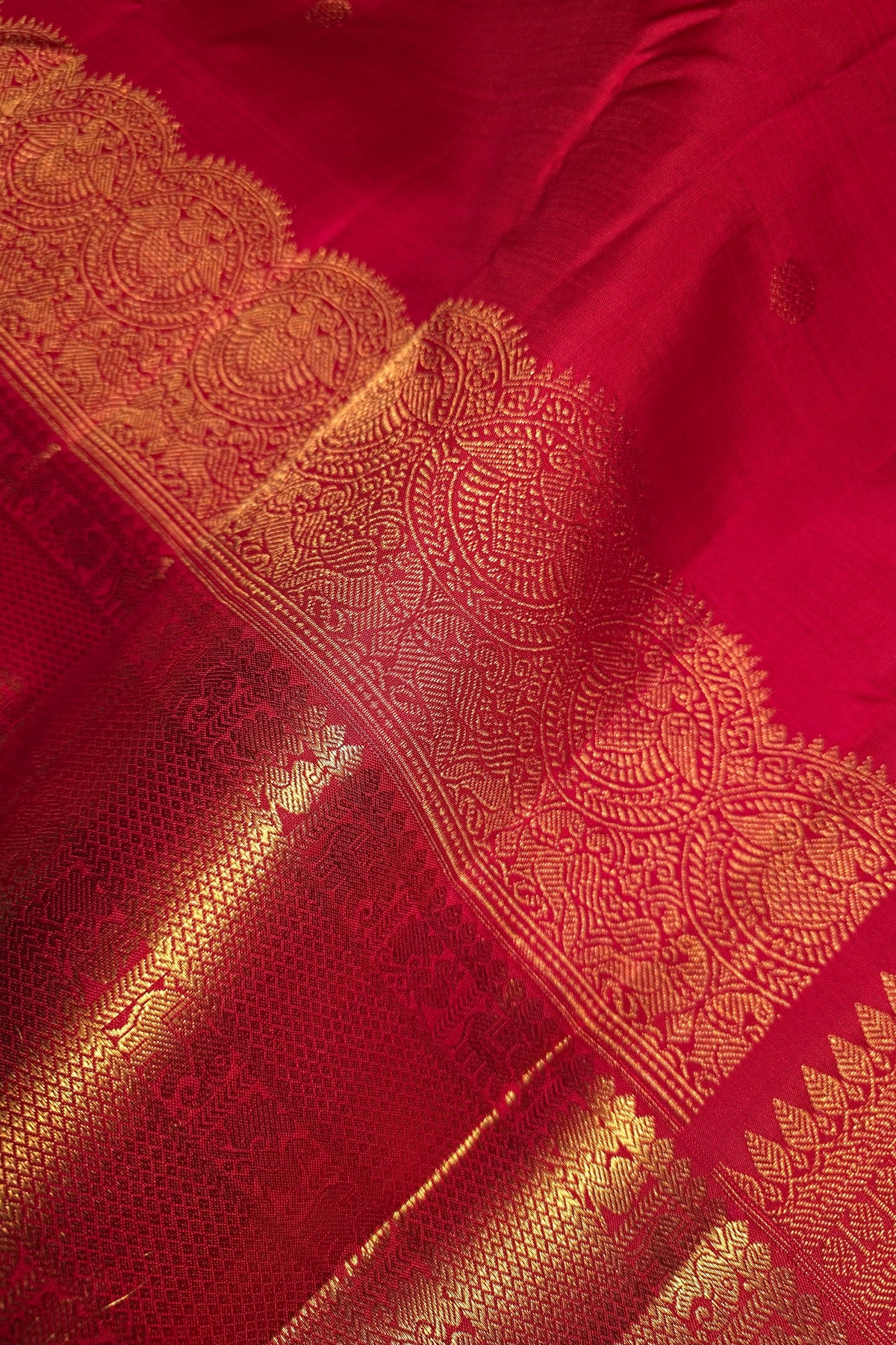 A close-up of a rich red fabric with an ornate gold woven border and metallic gold patterns.