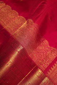A close-up of a rich red fabric with an ornate gold woven border and metallic gold patterns.