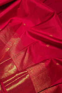 A close-up of a rich red silk saree with intricate gold zari brocade work and small gold motifs scattered across the fabric.