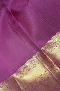 A close-up of a purple silk fabric, likely a saree, featuring a rich metallic gold zari border with intricate woven patterns.