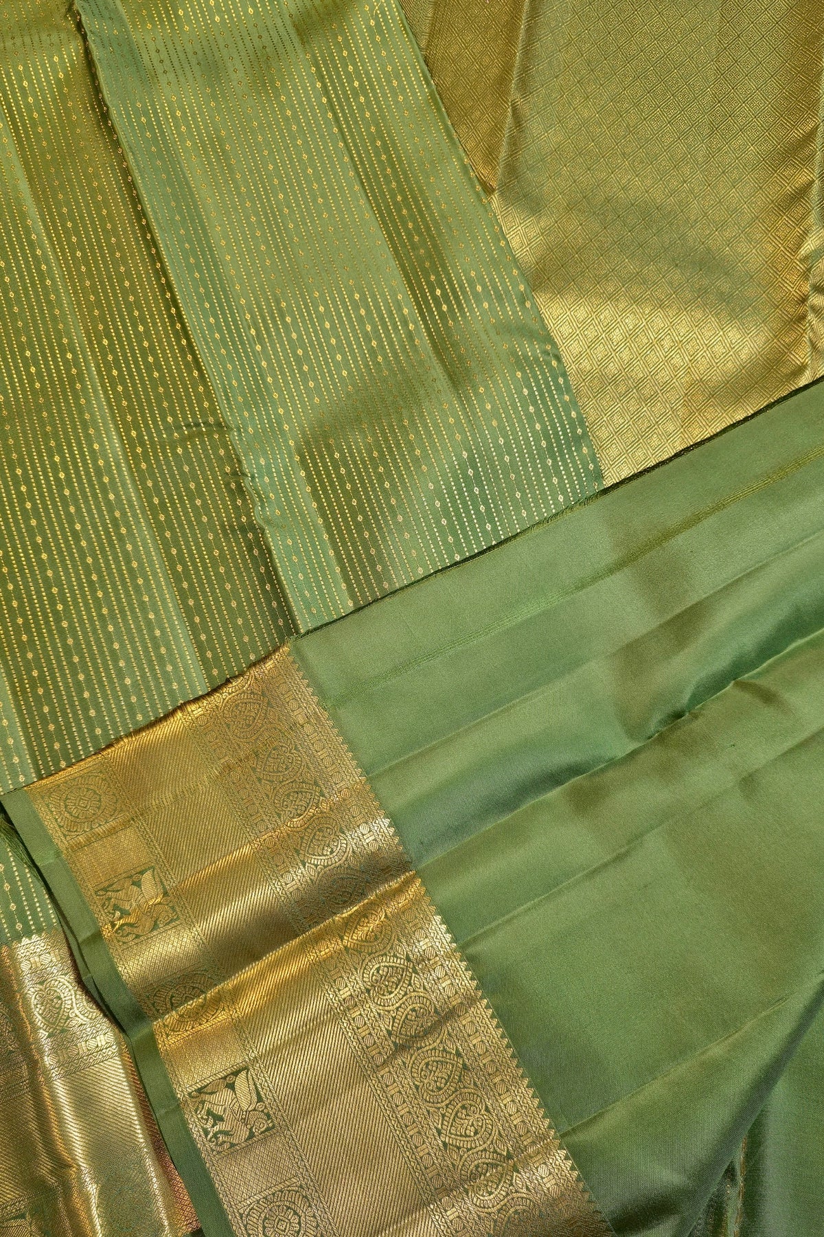 A close-up of a green and gold woven fabric, likely a sari, showing a green body with fine gold stripes and a wide gold zari border.