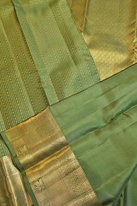 A close-up of a green and gold woven fabric, likely a sari, showing a green body with fine gold stripes and a wide gold zari border.