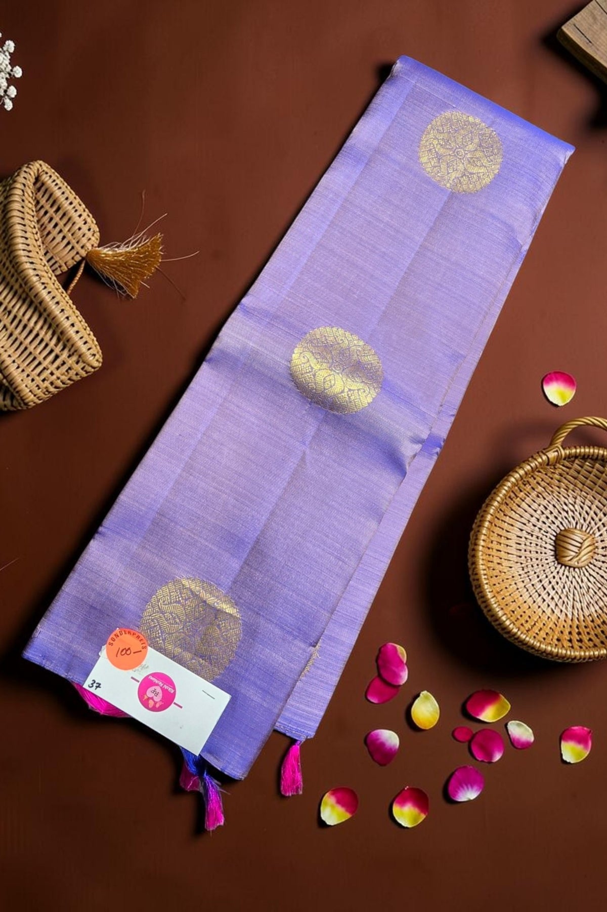 Purple fabric with gold patterns on a brown surface with wicker baskets and rose petals.