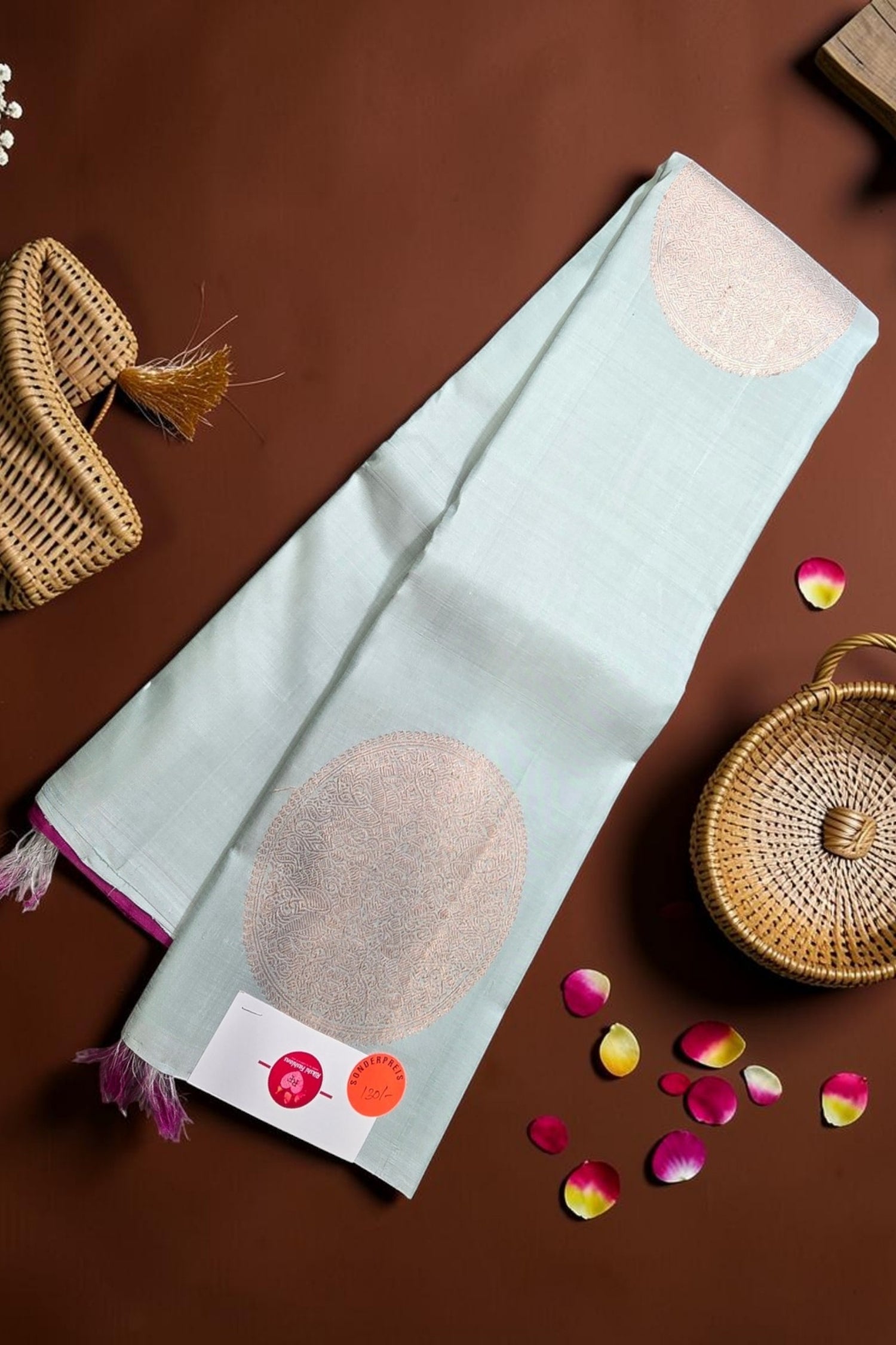 Light blue towel with beige circular designs on a brown surface with wicker baskets and rose petals.