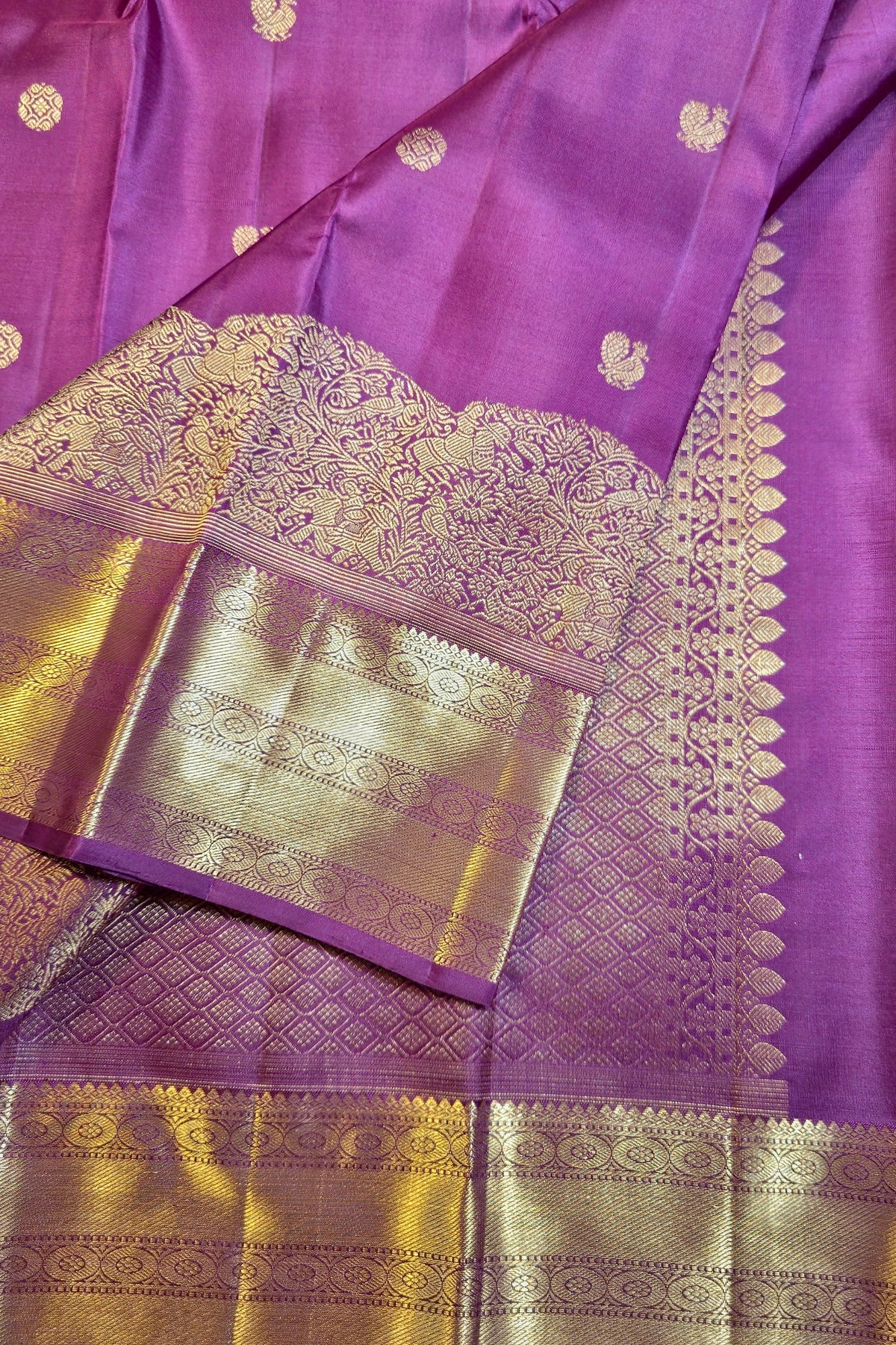 Purple silk saree with intricate gold zari woven patterns, featuring a wide decorative border and a matching gold-toned blouse piece.