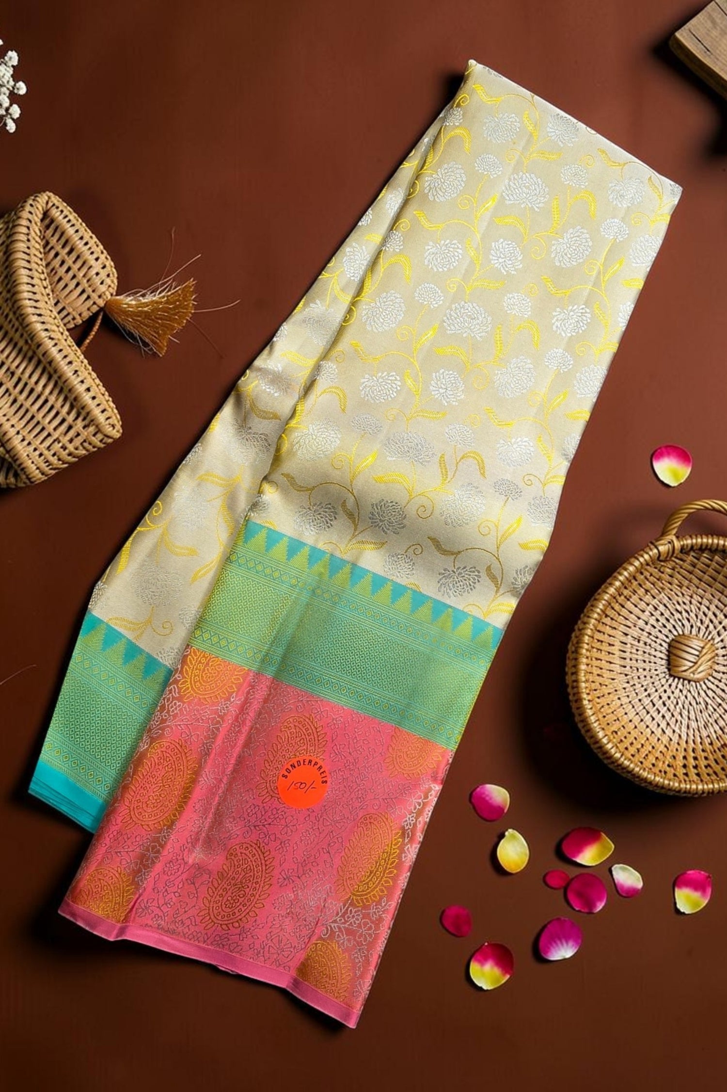 Colorful saree with floral patterns on a brown surface with baskets and petals.