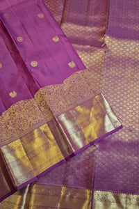 Purple silk saree with gold zari woven patterns and a wide decorative border, shown folded on a white background.