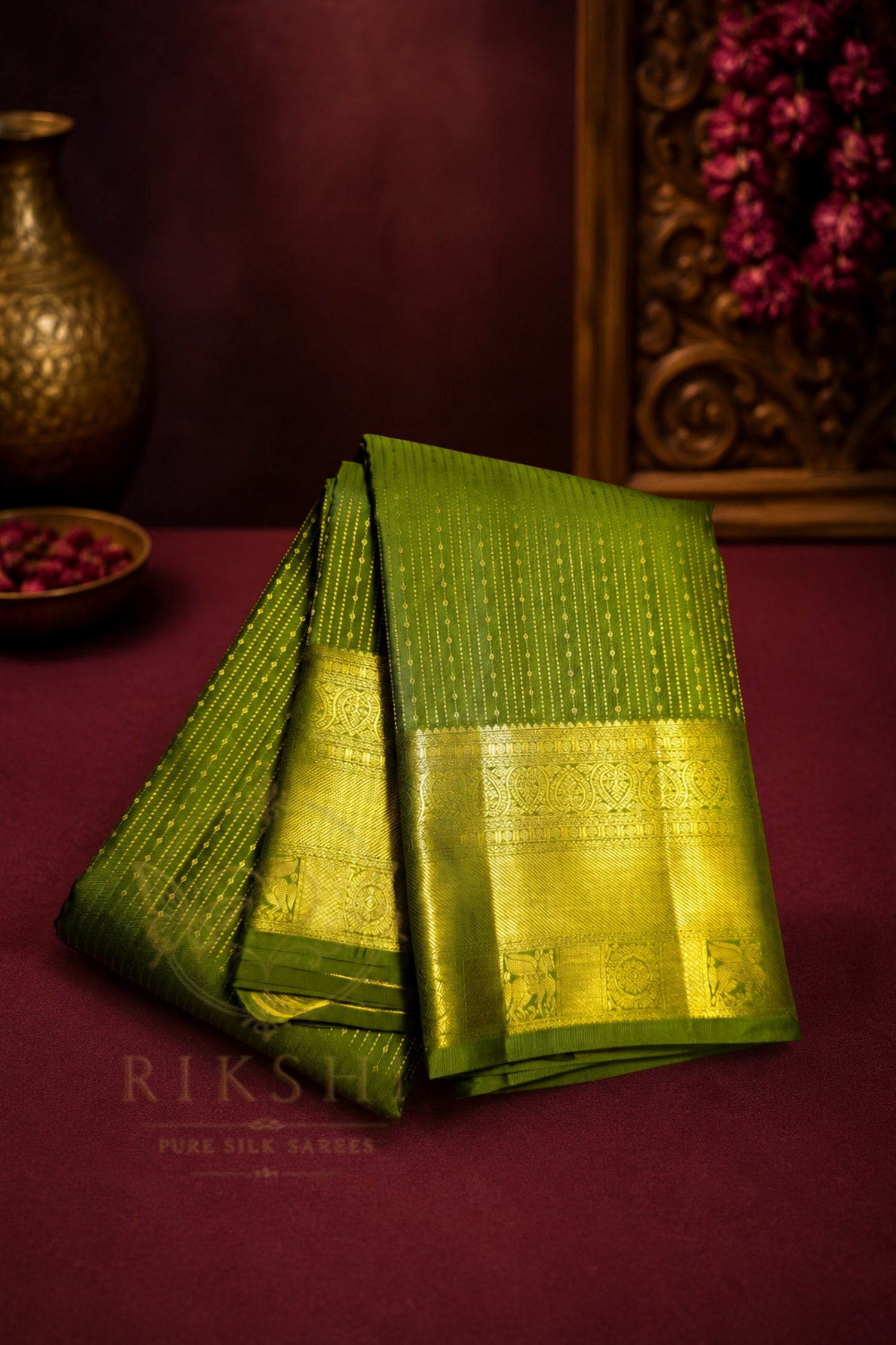 Green saree with gold zari border elegantly displayed on a maroon surface, showcasing its rich color and intricate design.