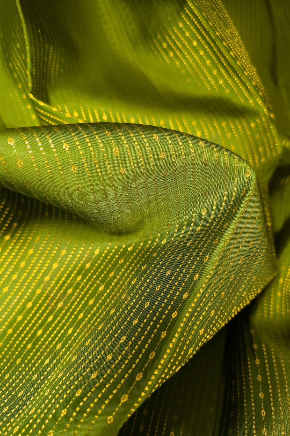 Close-up of green saree with gold zari border, showcasing intricate gold detailing on lush green fabric.