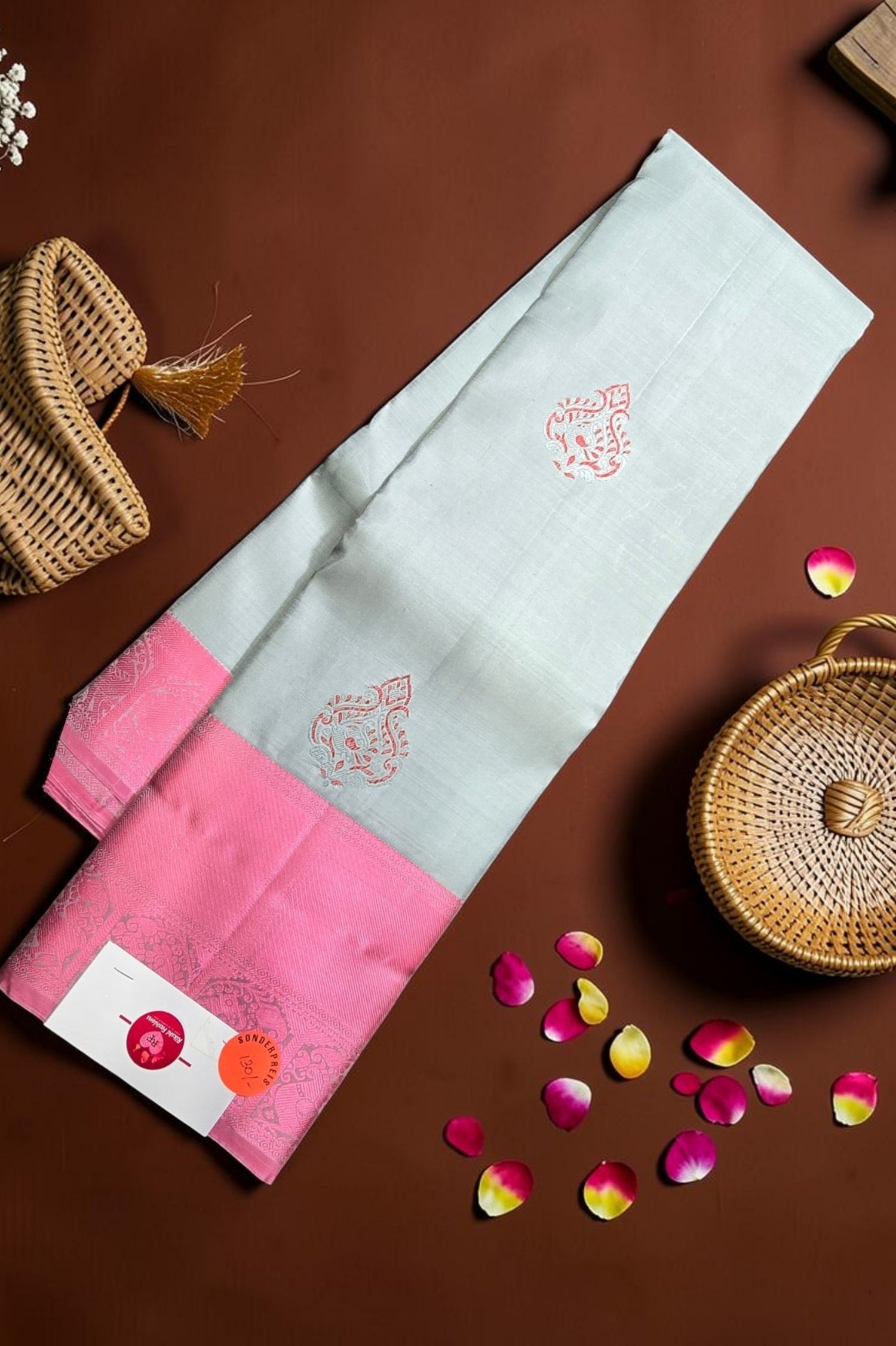Saree with pink and white design on a brown surface with wicker baskets and flower petals.