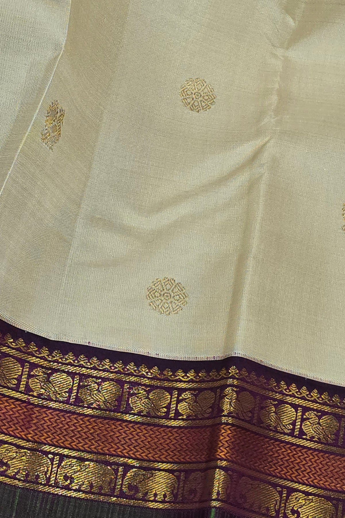 Close-up of a traditional saree with intricate gold patterns on a beige background