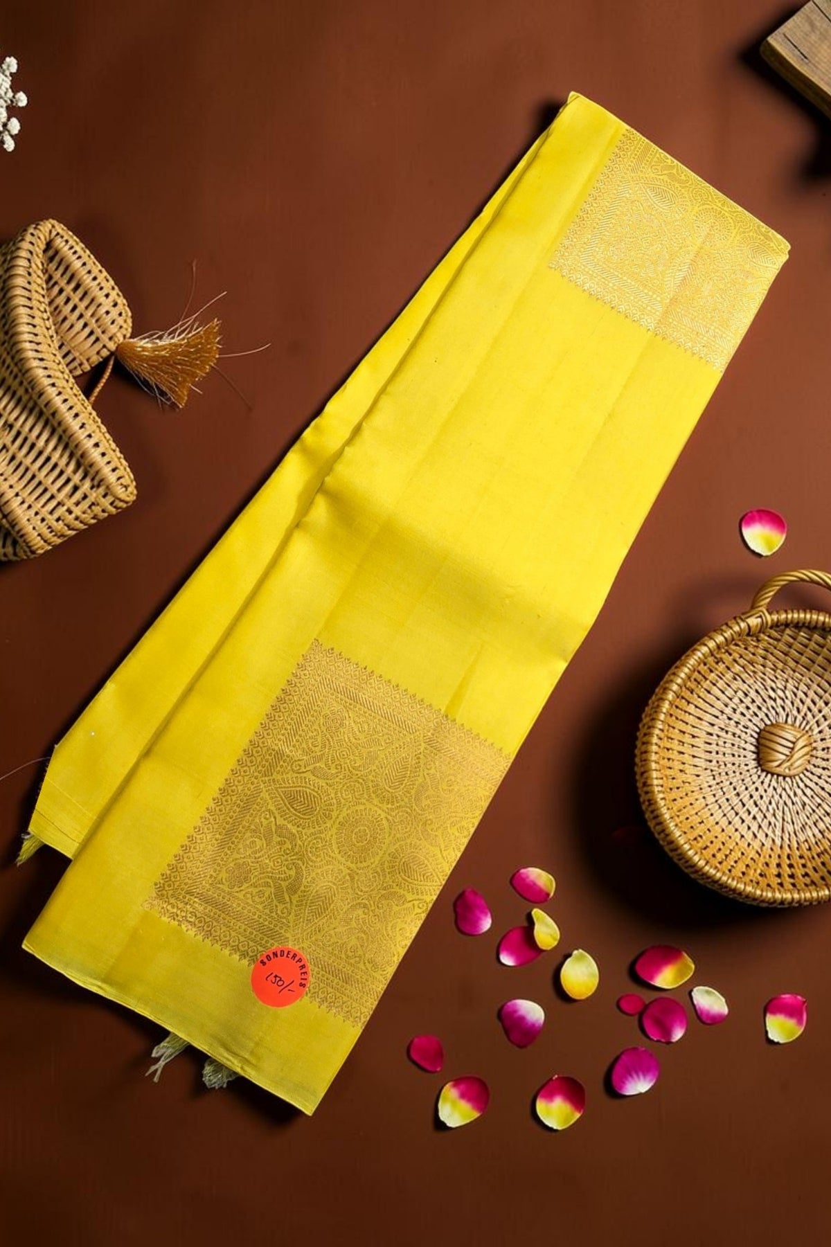 Yellow saree with gold border on a brown background with wicker baskets and rose petals.