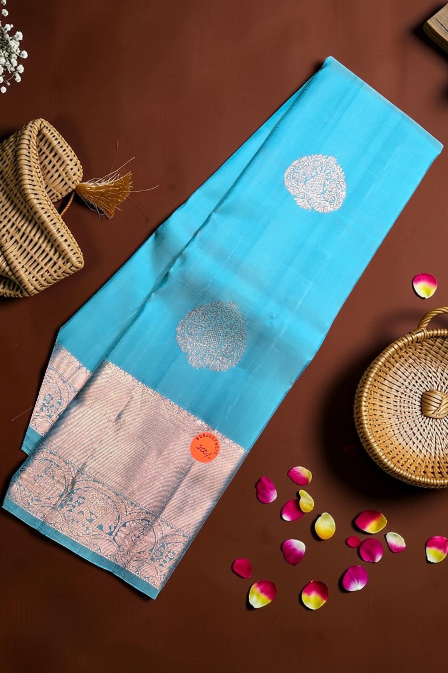 Blue fabric with white patterns on a brown surface with wicker baskets and flower petals.