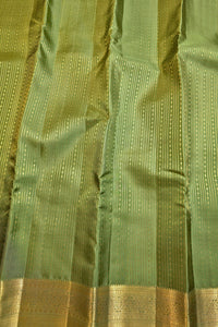 A close-up of a green silk fabric, likely a sari, featuring vertical stripes of small gold dots and a wide gold zari border at the bottom.