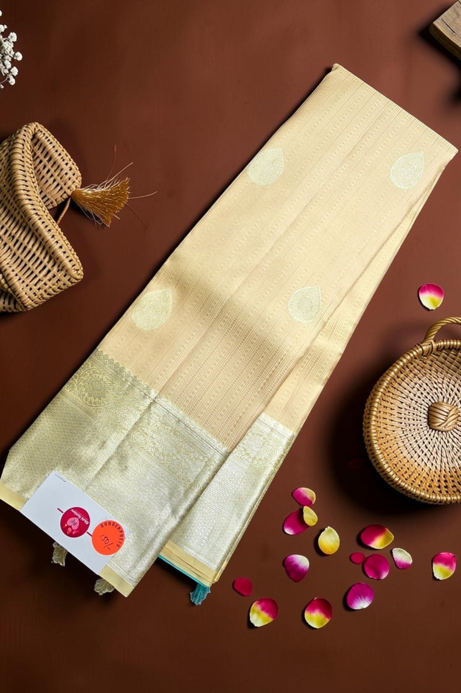 Beige saree with gold border on a brown background with wicker baskets and rose petals.