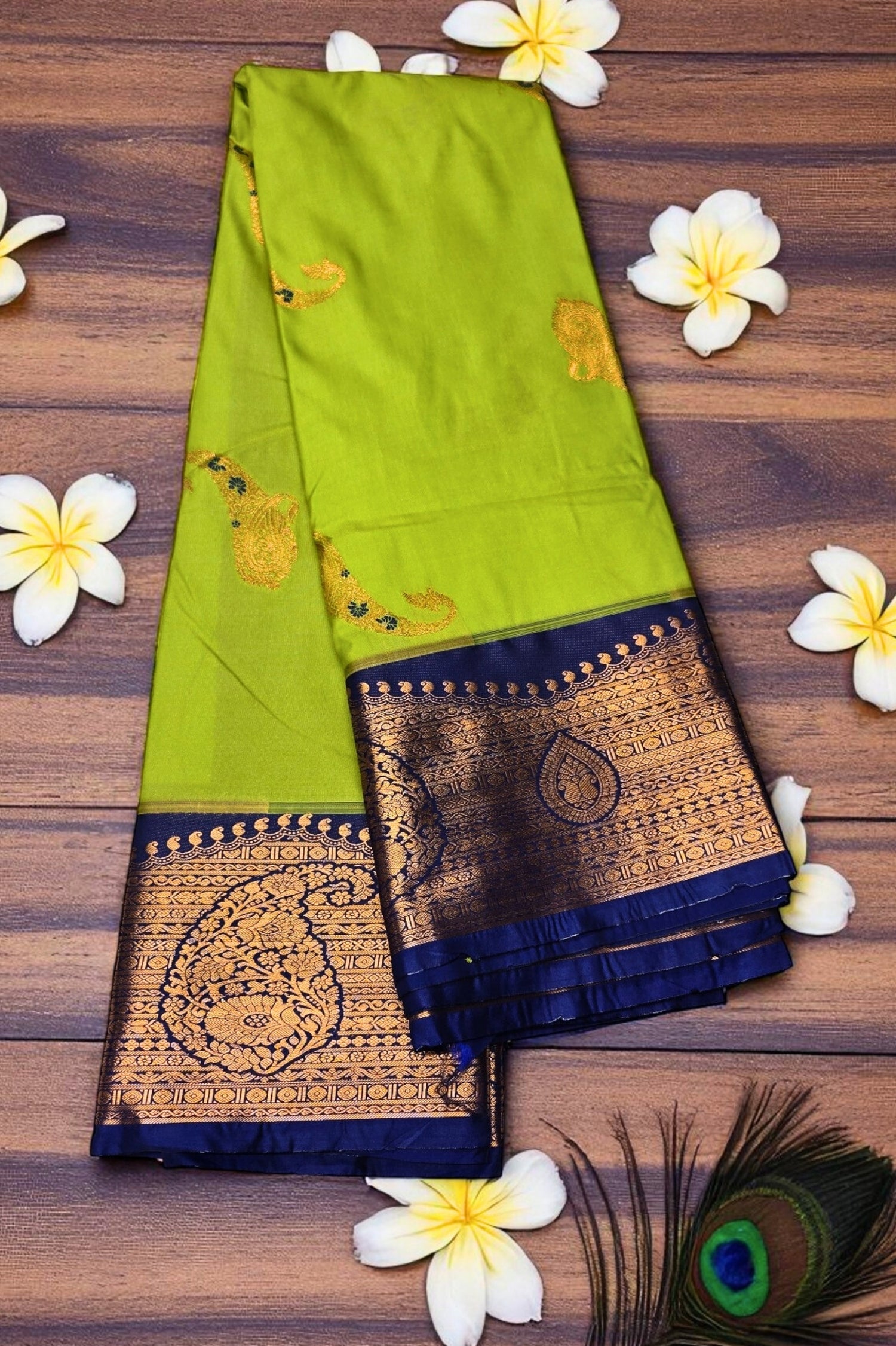 Green saree with gold and blue border on a wooden surface with flowers