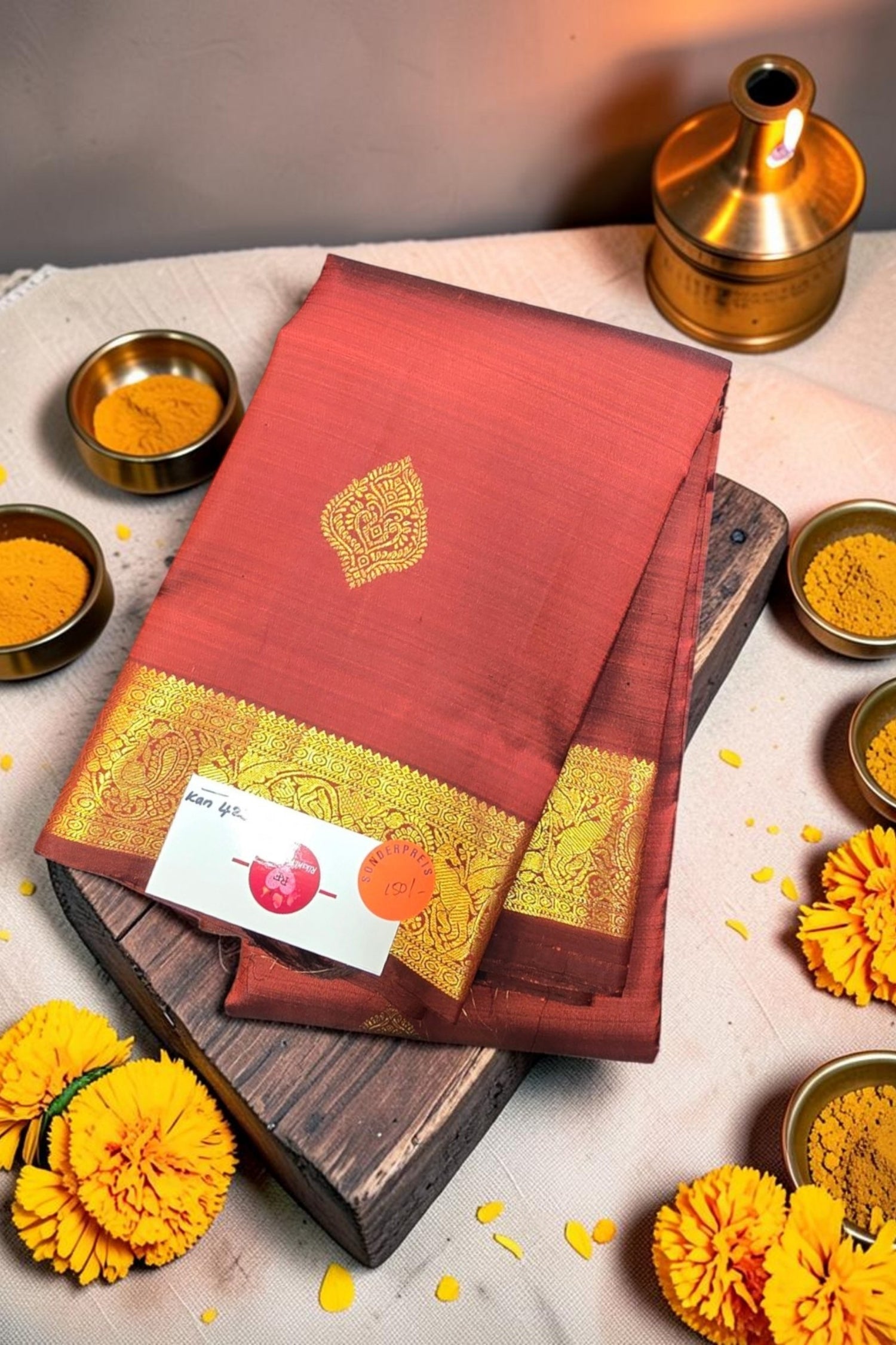 Red saree with gold border on a wooden board, surrounded by yellow flowers and small bowls.