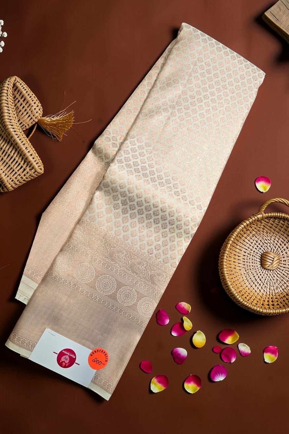 Beige towel with a pattern on a brown surface with wicker baskets and flower petals.