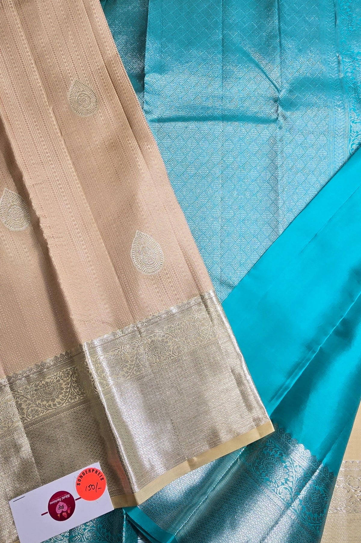 Close-up of a saree with a beige border and blue fabric, featuring a brand label.