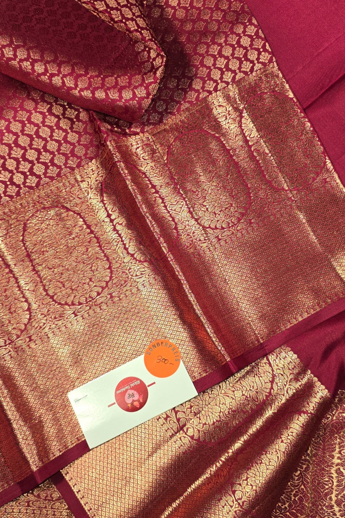 Close-up of a maroon fabric with intricate patterns and a brand label.