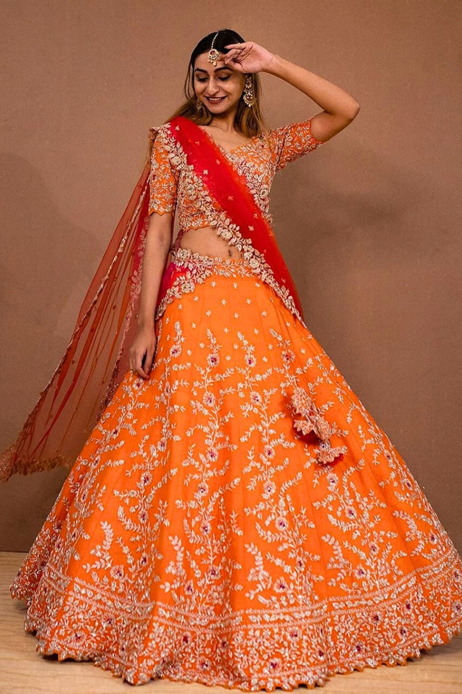 Woman wearing an orange and red traditional outfit against a brown background