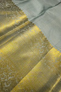 light sage green silk saree with a wide ornate gold zari border showing intricate design and luxurious texture.