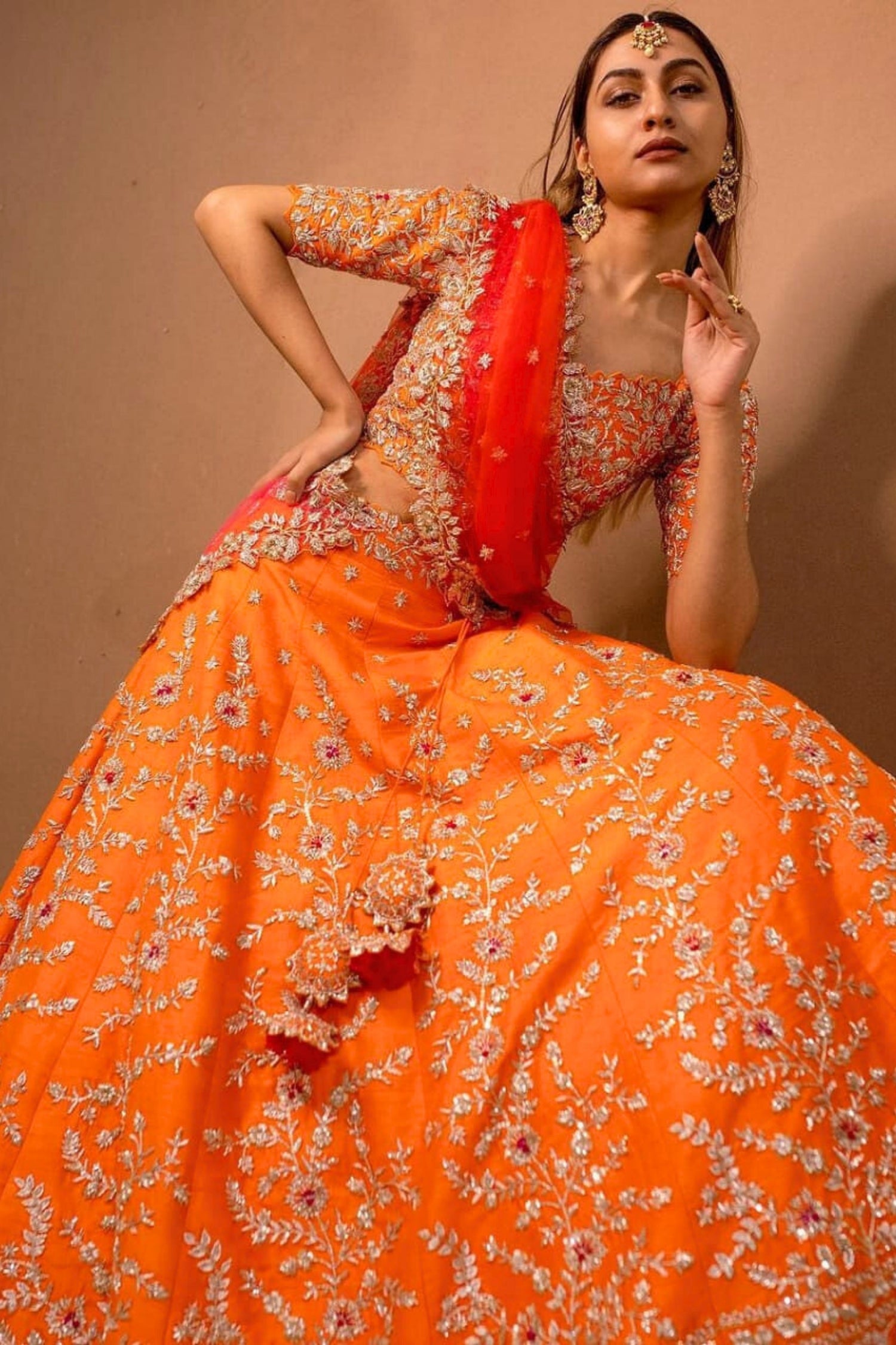 Woman wearing an orange and red traditional outfit with floral patterns against a beige background