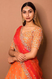 Woman wearing an orange and red traditional outfit with intricate designs against a brown background