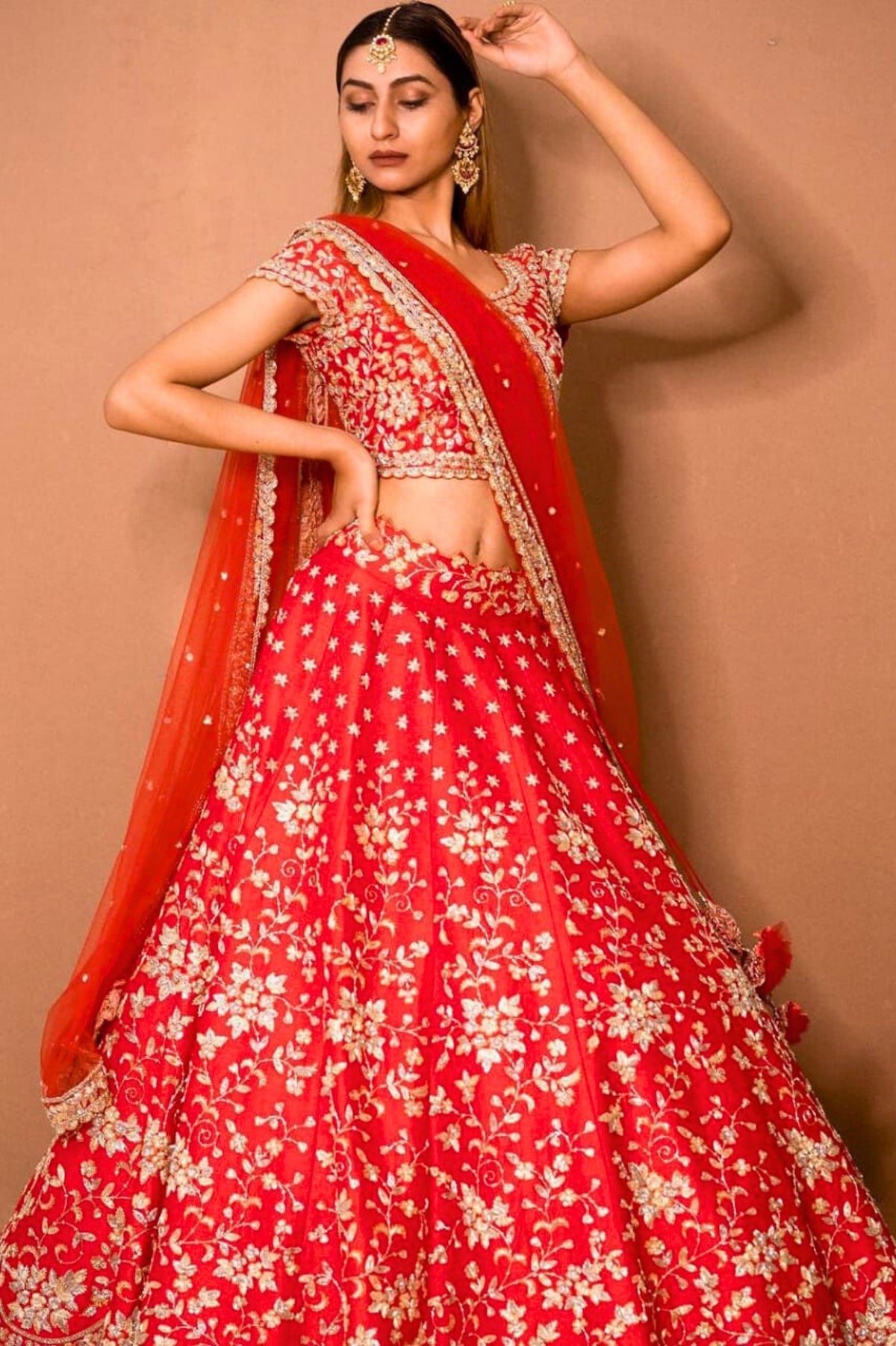 Woman wearing a red floral lehenga with a matching dupatta against a beige background