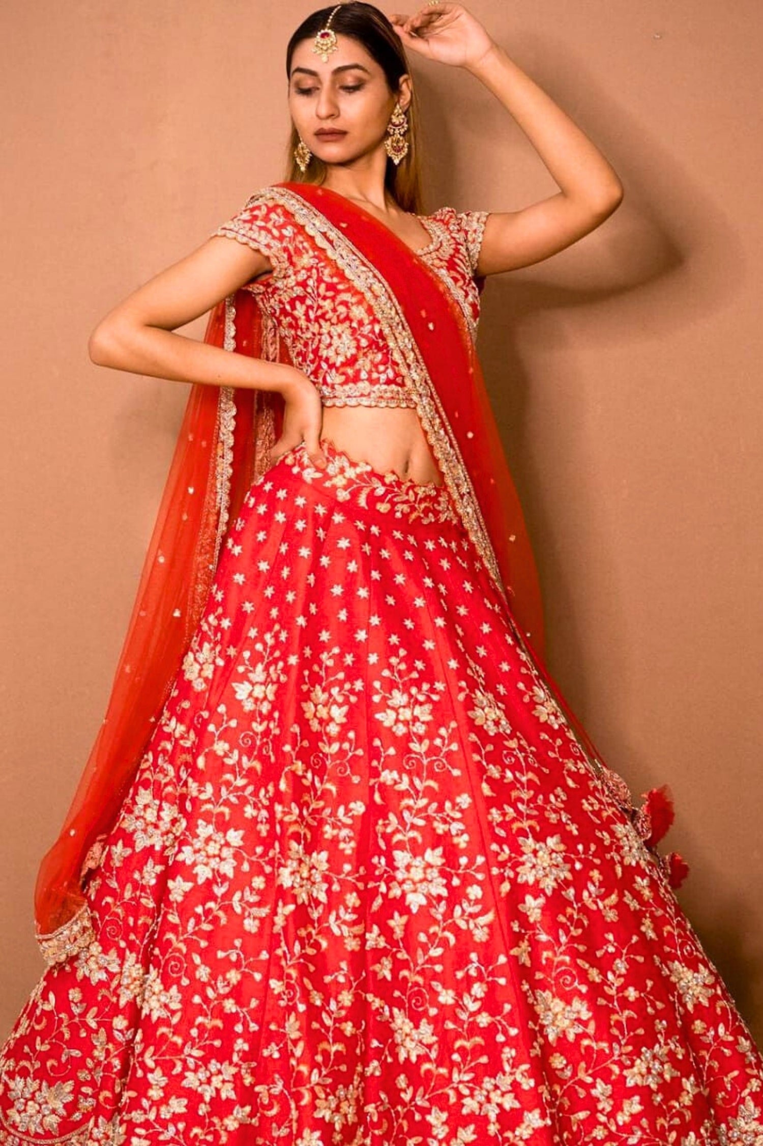 Woman wearing a red floral lehenga with a matching dupatta against a beige background