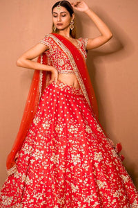 Woman wearing a red floral lehenga with a matching dupatta against a beige background