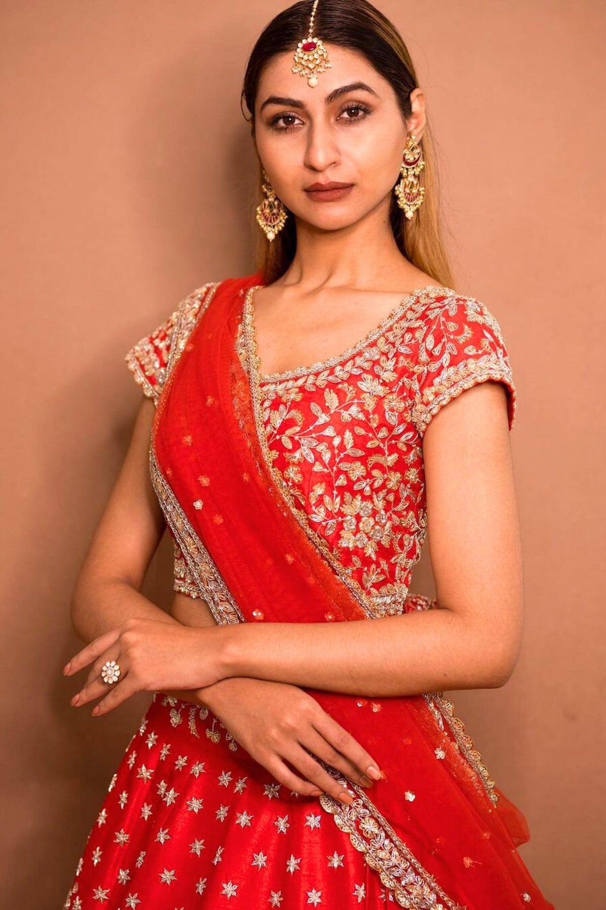 Woman wearing a red traditional outfit with gold embroidery against a beige background