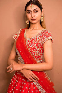 Woman wearing a red traditional outfit with gold embroidery against a beige background