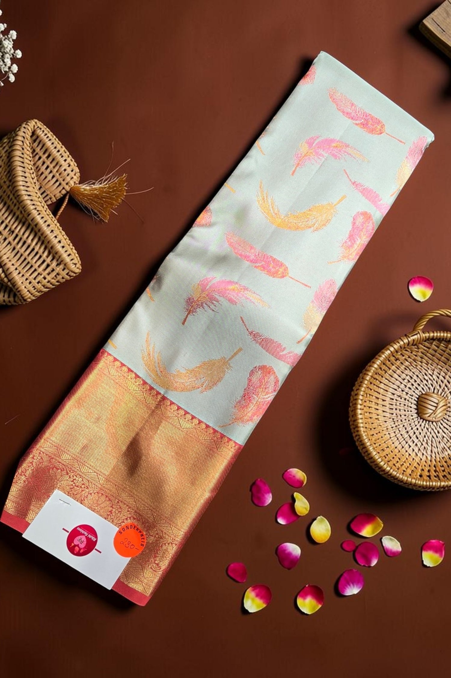 Fabric with floral pattern on a brown surface with wicker baskets and rose petals.