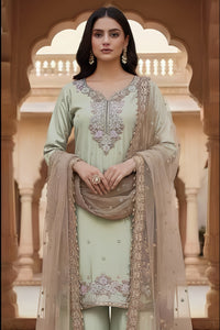 Woman in a light green traditional outfit with intricate embroidery, standing in front of an architectural background.