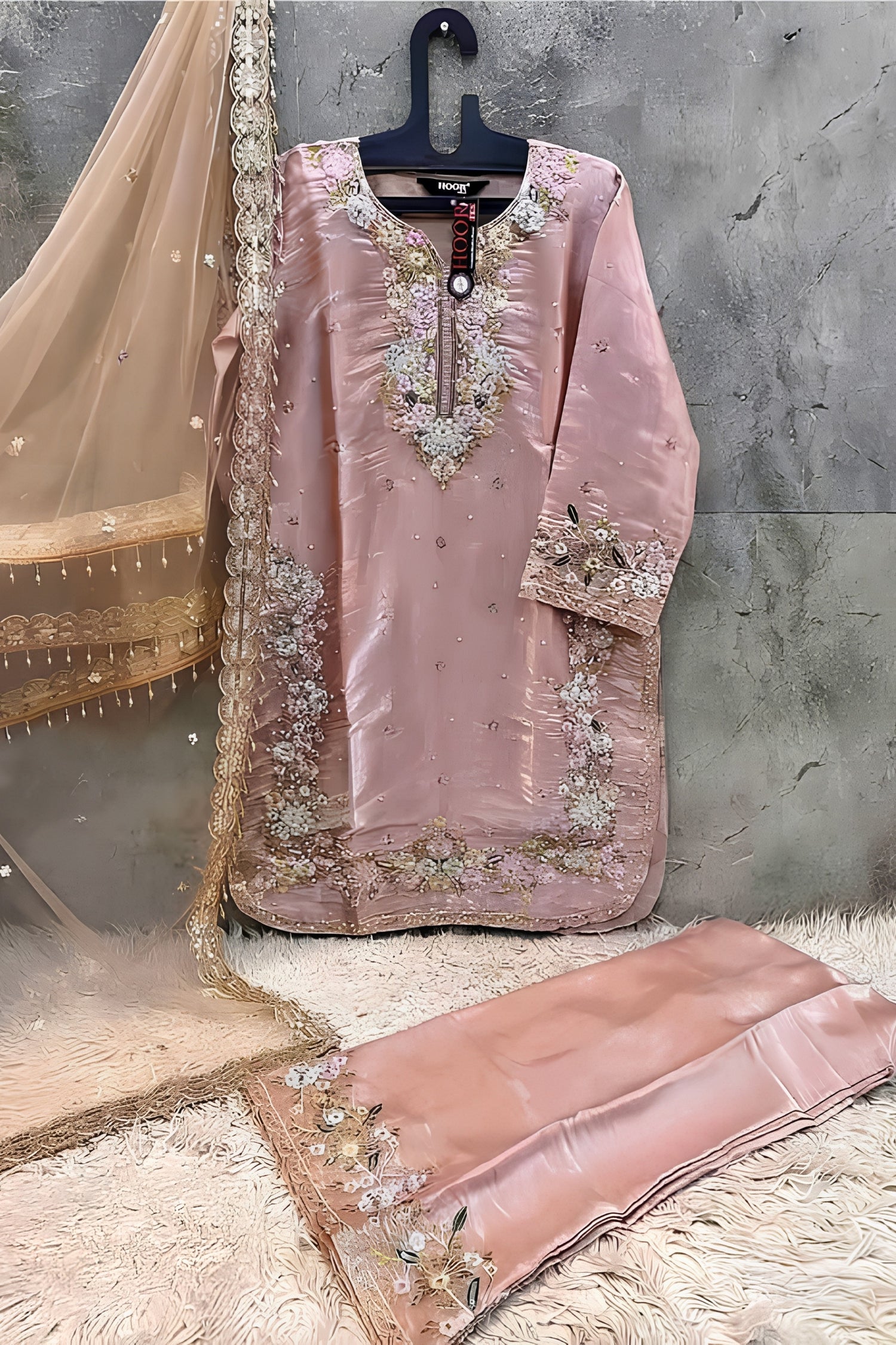 Pink embroidered traditional outfit with a hanger on a textured surface