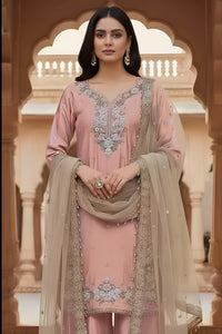 Woman in a traditional pink and beige outfit with intricate designs, standing in an ornate architectural setting.