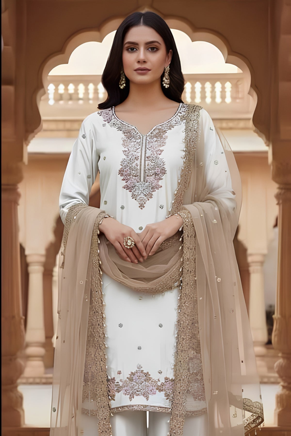 Woman in traditional white and beige embroidered outfit standing in a decorative architectural setting.