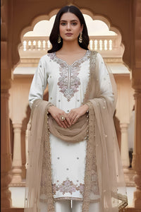 Woman in traditional white and beige embroidered outfit standing in a decorative architectural setting.