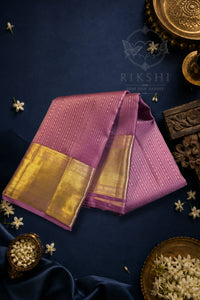 Royal Purple Silk Saree with Wide Gold Zari Border draped elegantly against a dark background adorned with flowers.