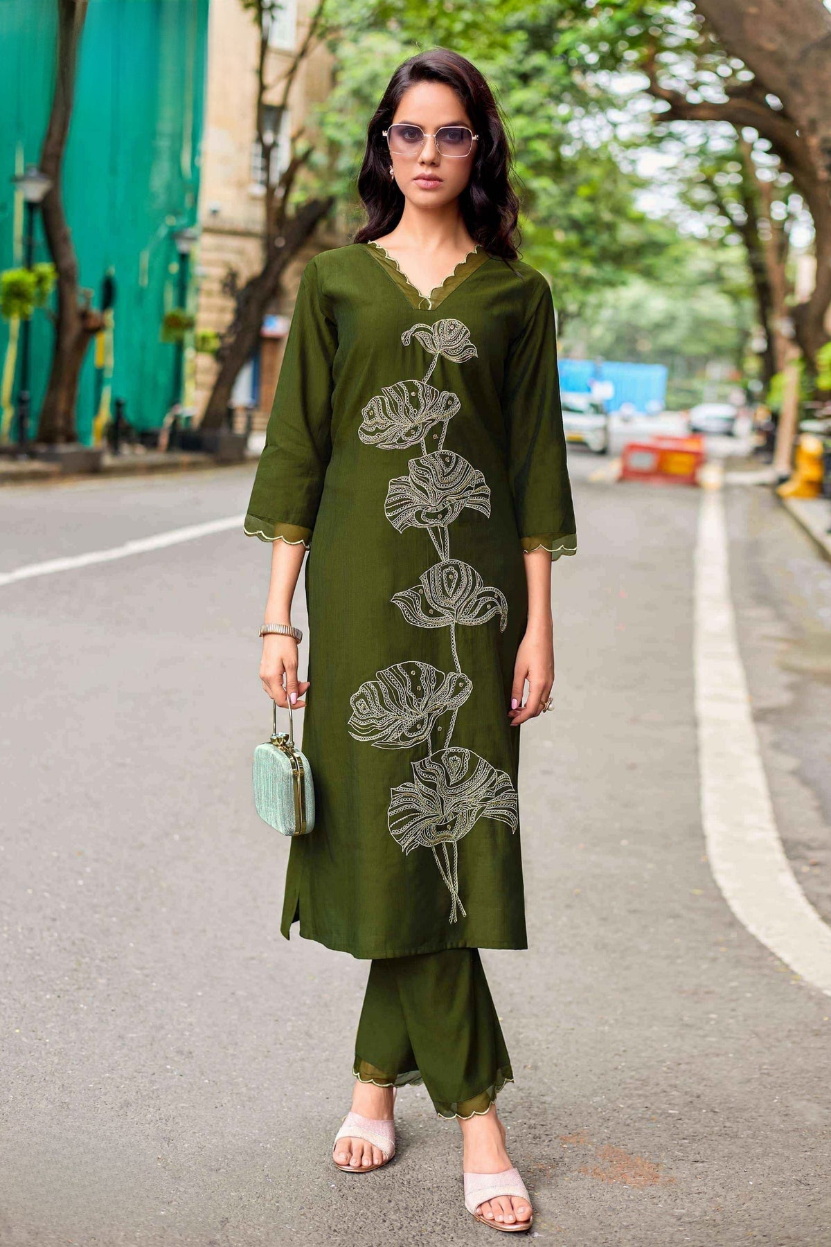 Woman in a green outfit with leaf patterns standing on a street.