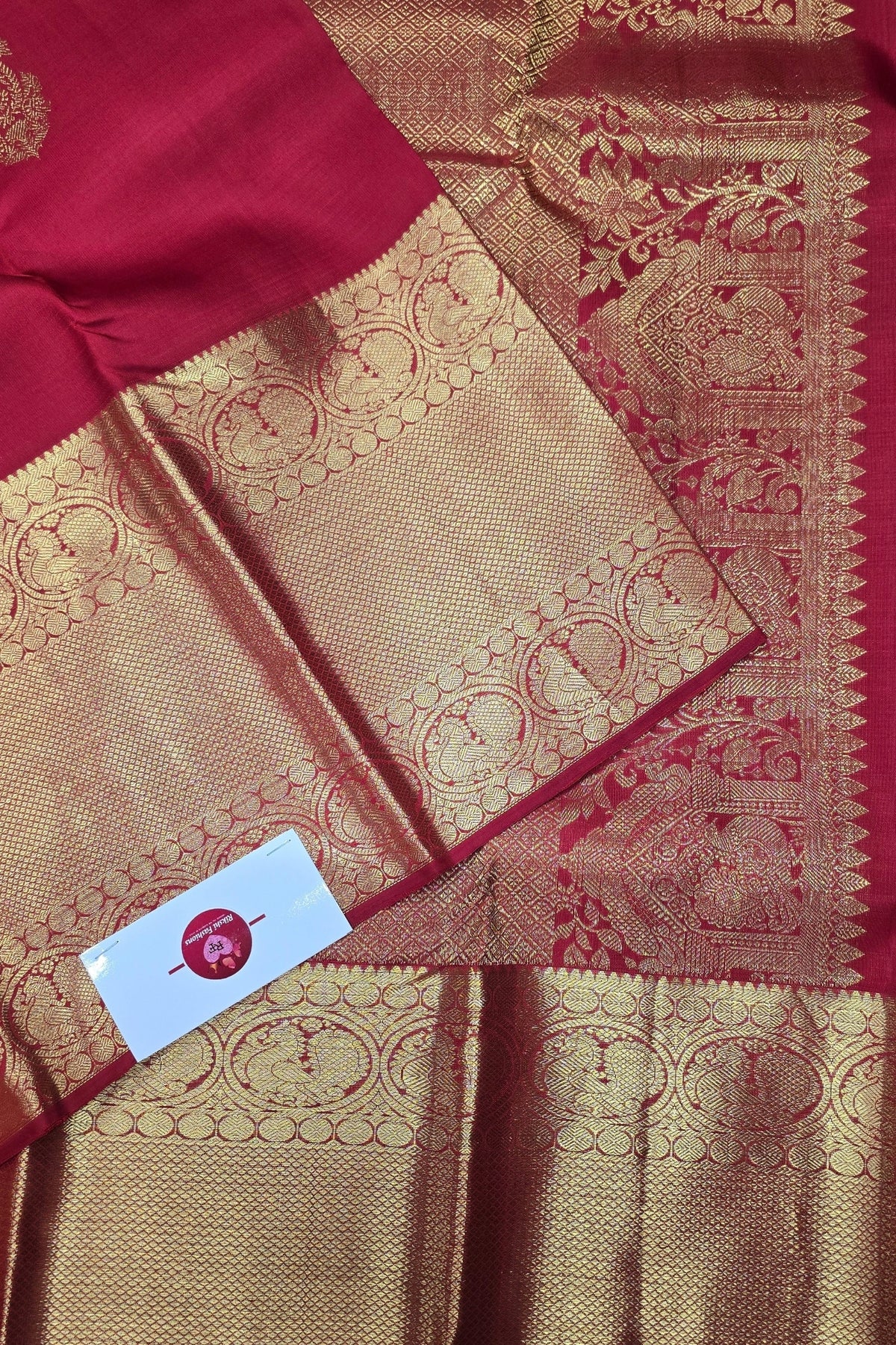 Red and gold saree with intricate patterns and a visible brand label.