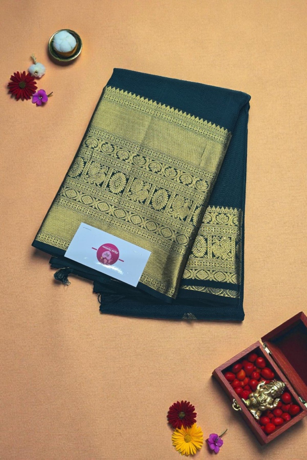 Black and gold saree with a decorative box and flowers on a beige background