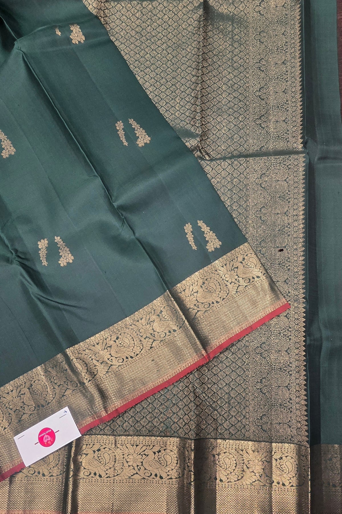 Teal saree with gold border and a visible brand label.