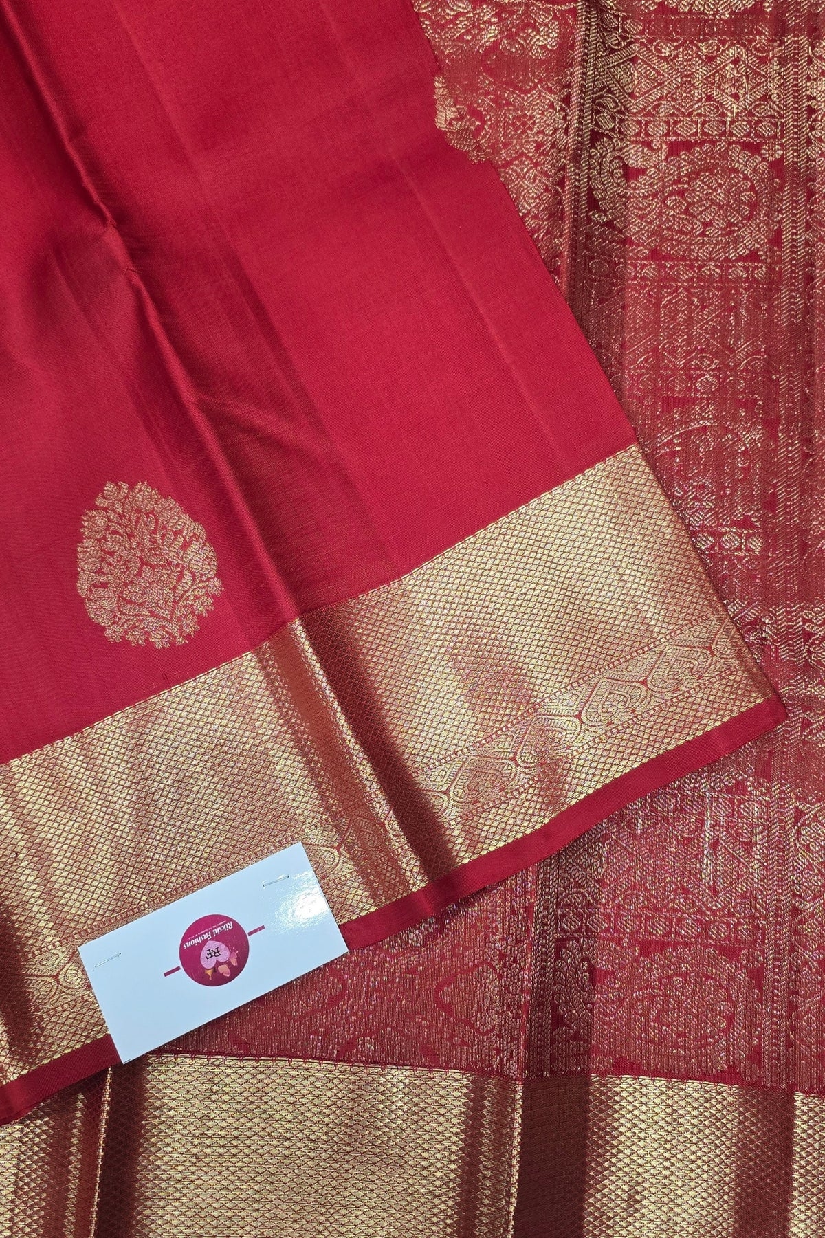 Red and gold saree with a visible brand label on a textured background