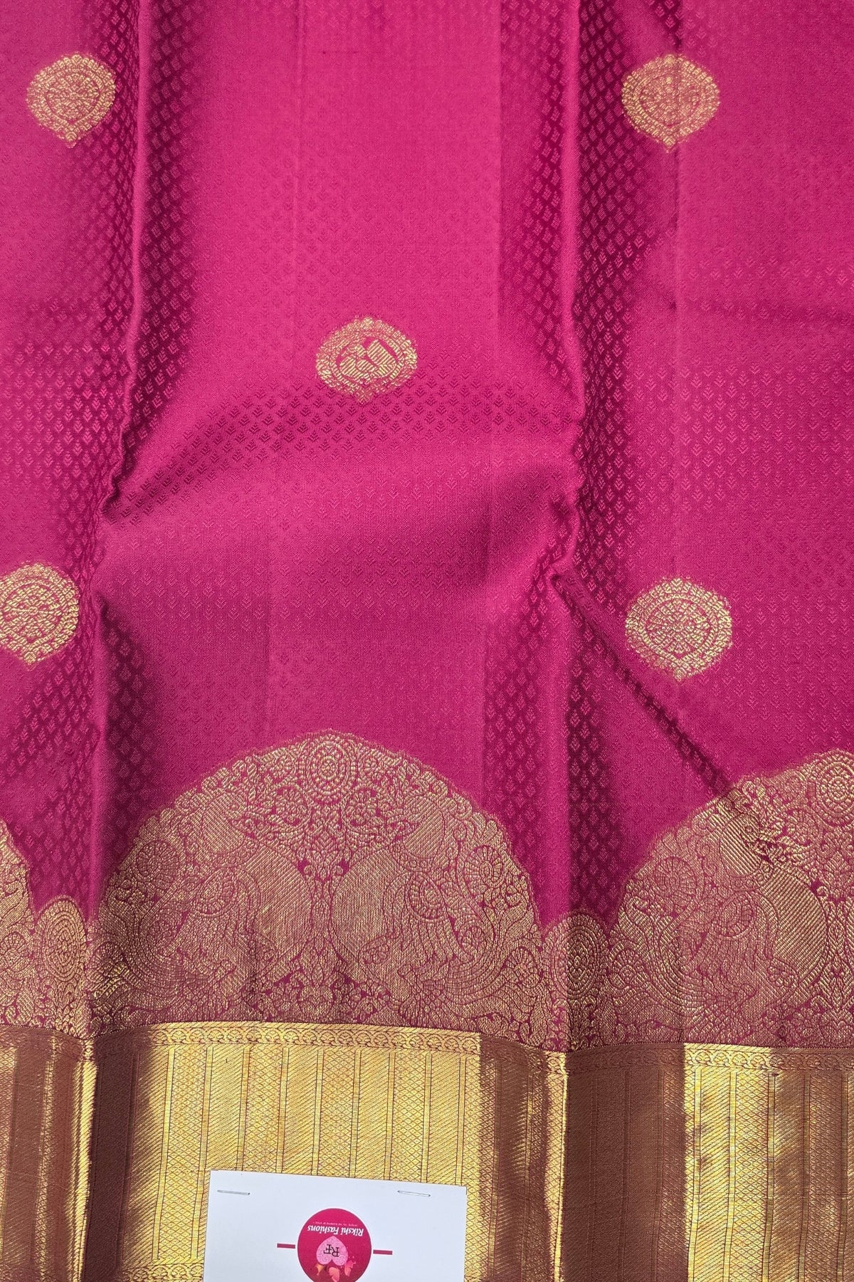 Pink saree with gold border and patterns, featuring a brand label.