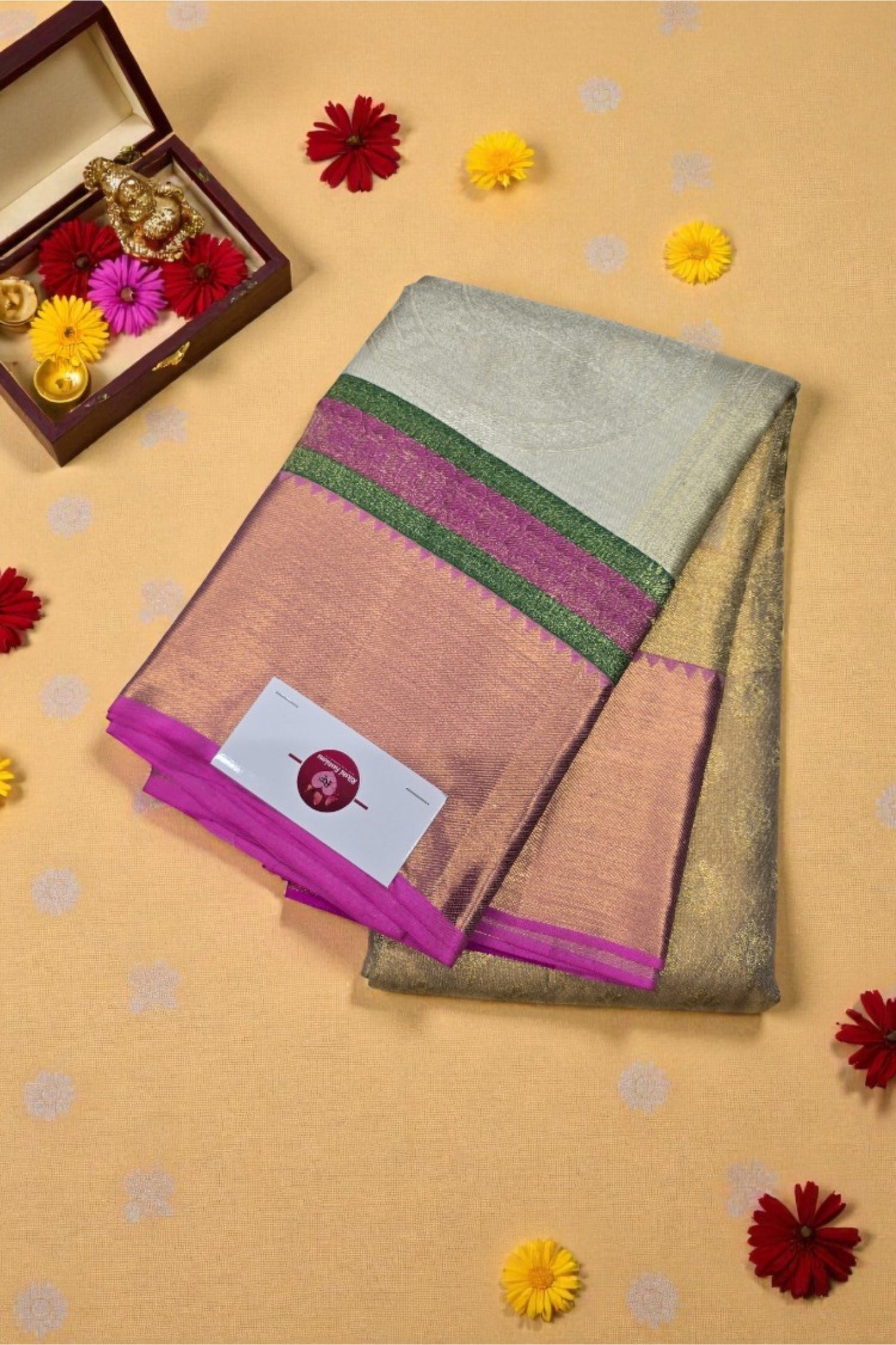 Folded saree with a visible brand label on a beige background with decorative flowers.