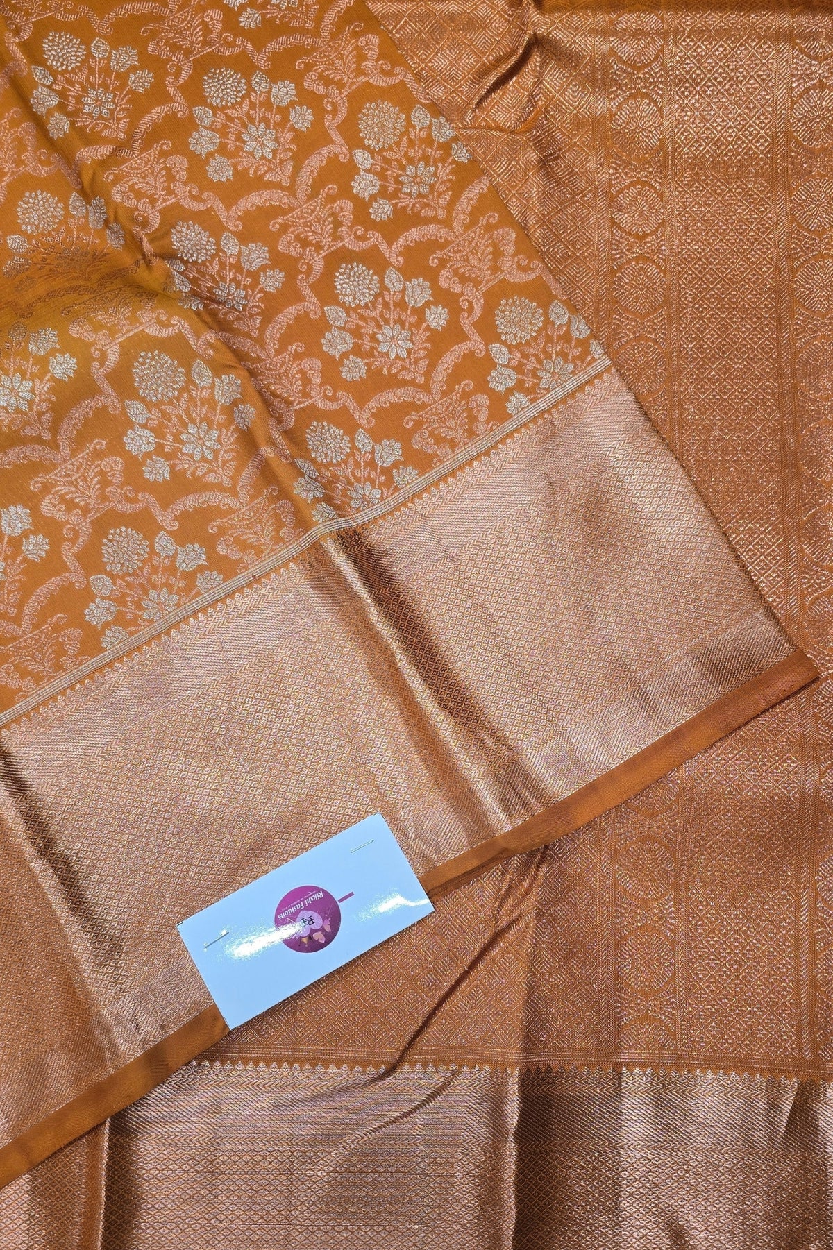 Brown saree with floral patterns and a visible brand label.